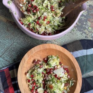 single serving of shaved brussels sprout salad in a wooden bowl next to a serving bowl of salad