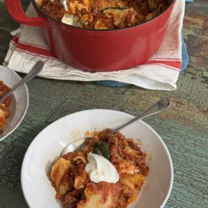 one pot lasagna in a dutch oven with a single serving of lasagna in front of it