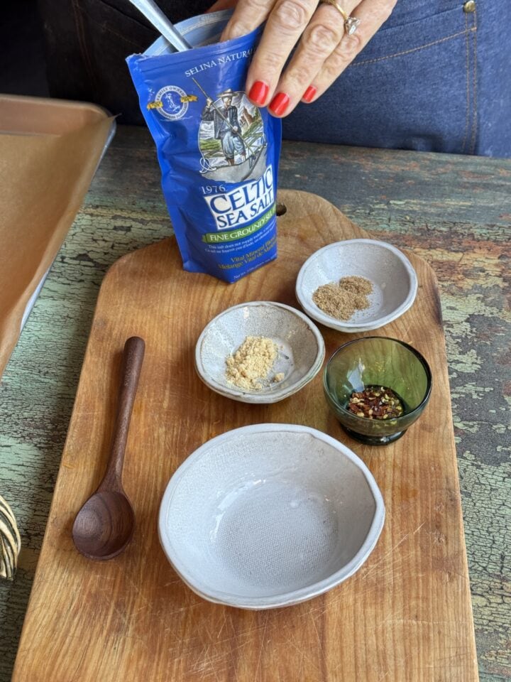 a cutting board with small bowls of spices on it and a bag of celtic sea salt