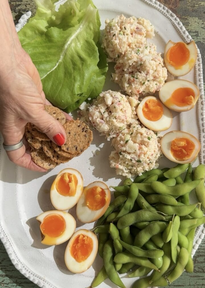 teri adding cracker to a platter with soy marinated eggs and shrimp salad