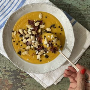 a bowl of pumpkin soup with toppings and a spoonful of soup held above the bowl