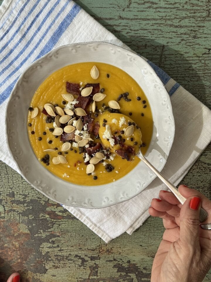 a bowl of pumpkin soup with toppings and a spoonful of soup held above the bowl