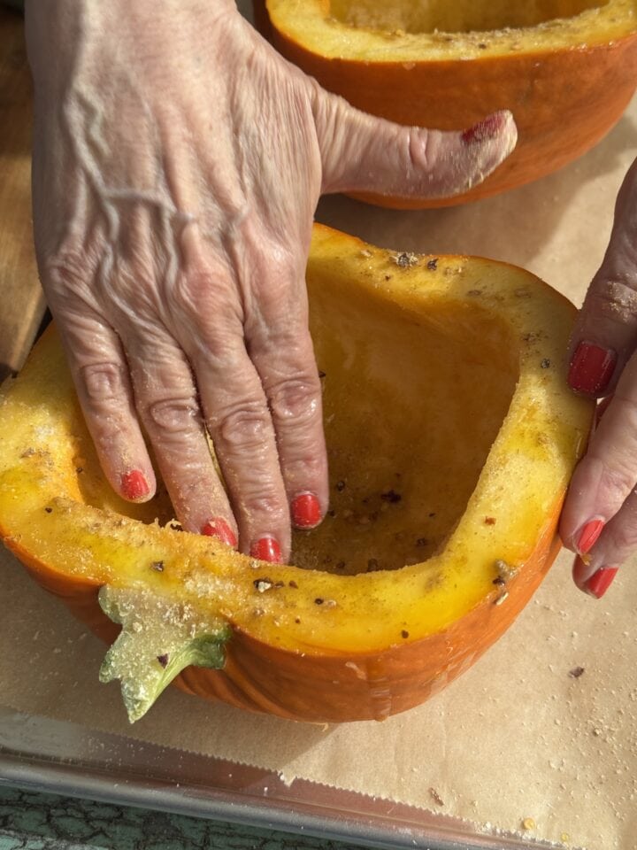 a hand rubbing oil onto pumpkin with seasoning on it